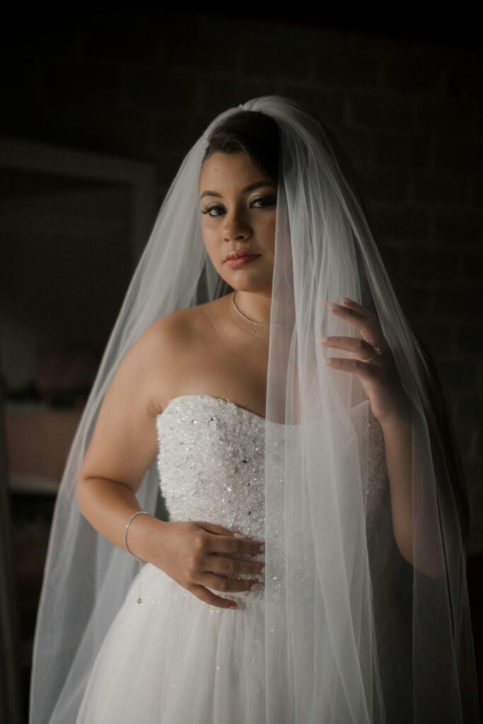 Brud i vit klanning med sloja fotograferad i mjukt ljus.