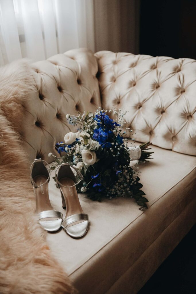 Brudskor och brudbukett placerade pa sammetssoffa.