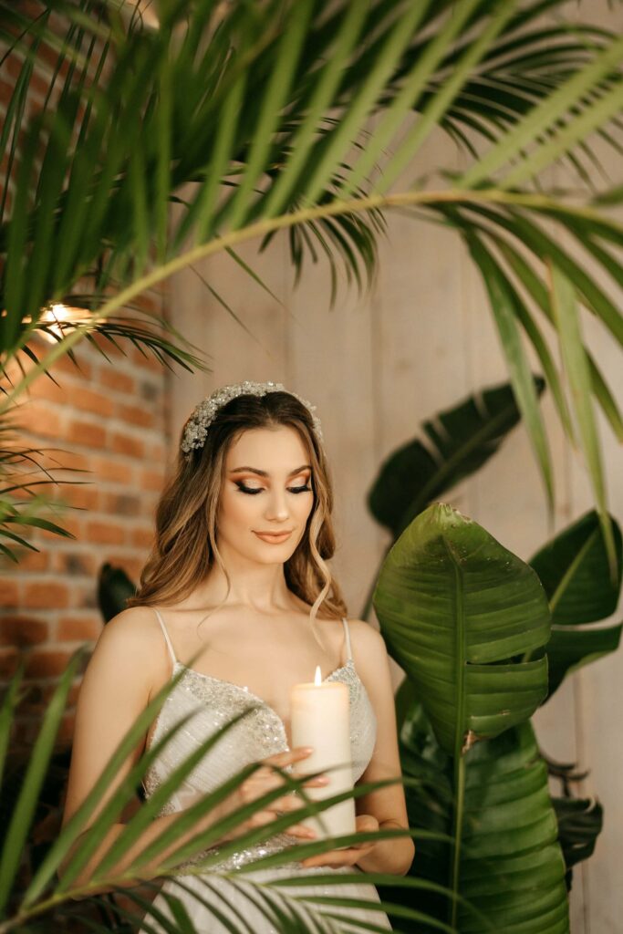 Brud håller ett levande ljus omgiven av gröna växter