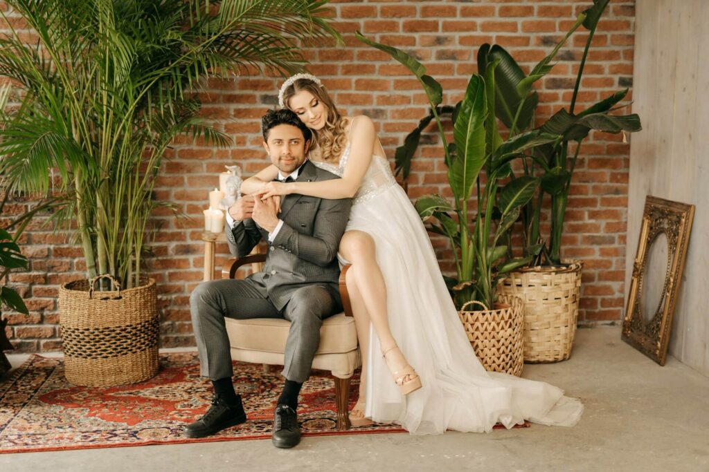 Brud och brudgum poserar framför tegelvägg och gröna växter