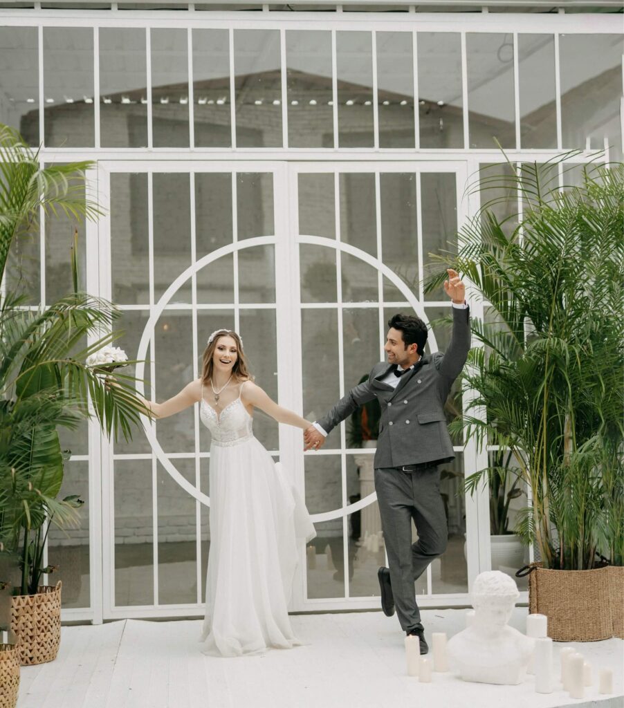 Brud och brudgum håller händer och skrattar framför stora fönster