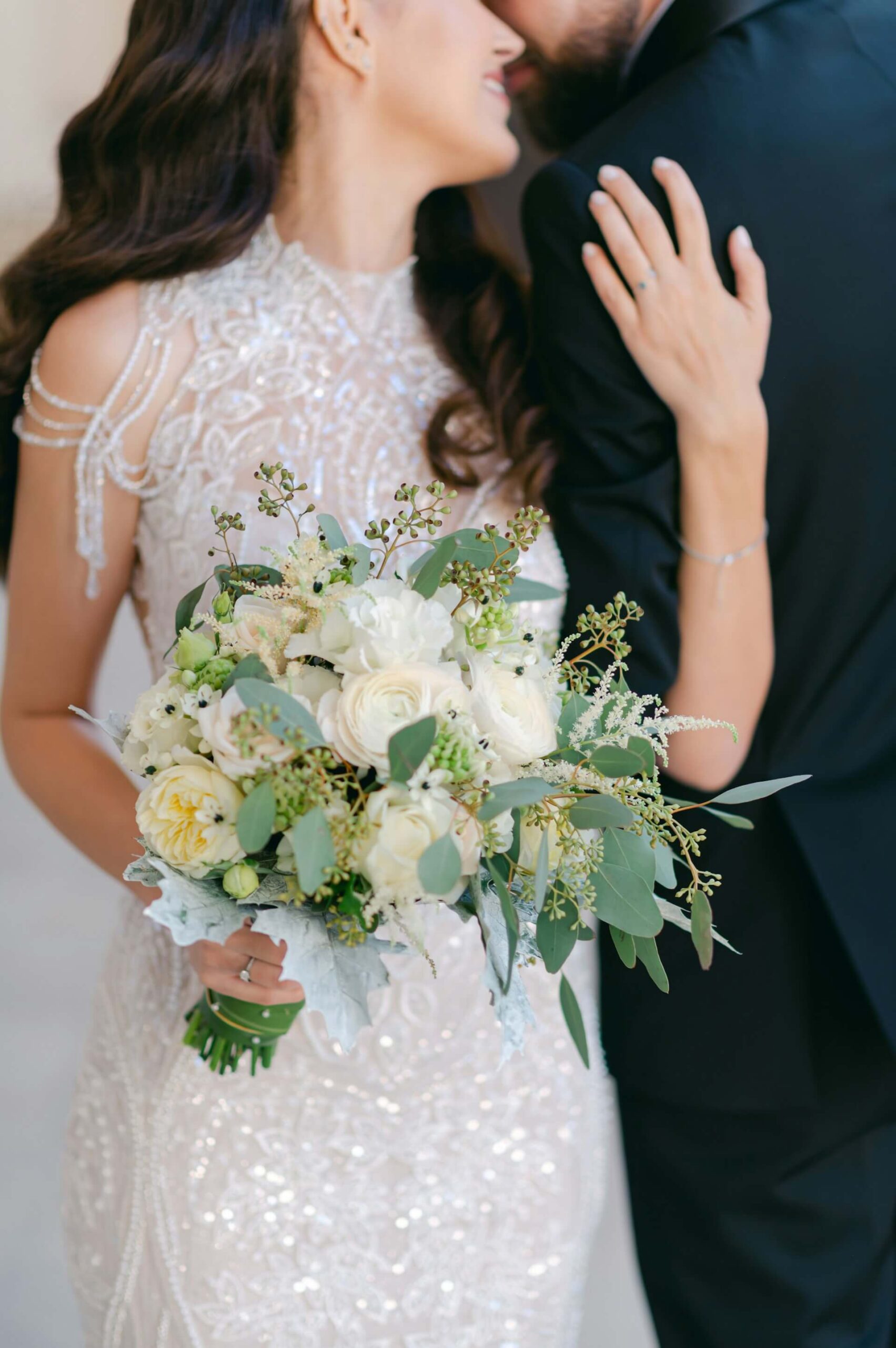 Närbild av brud som håller en bukett med vita rosor medan brudgummen står intill