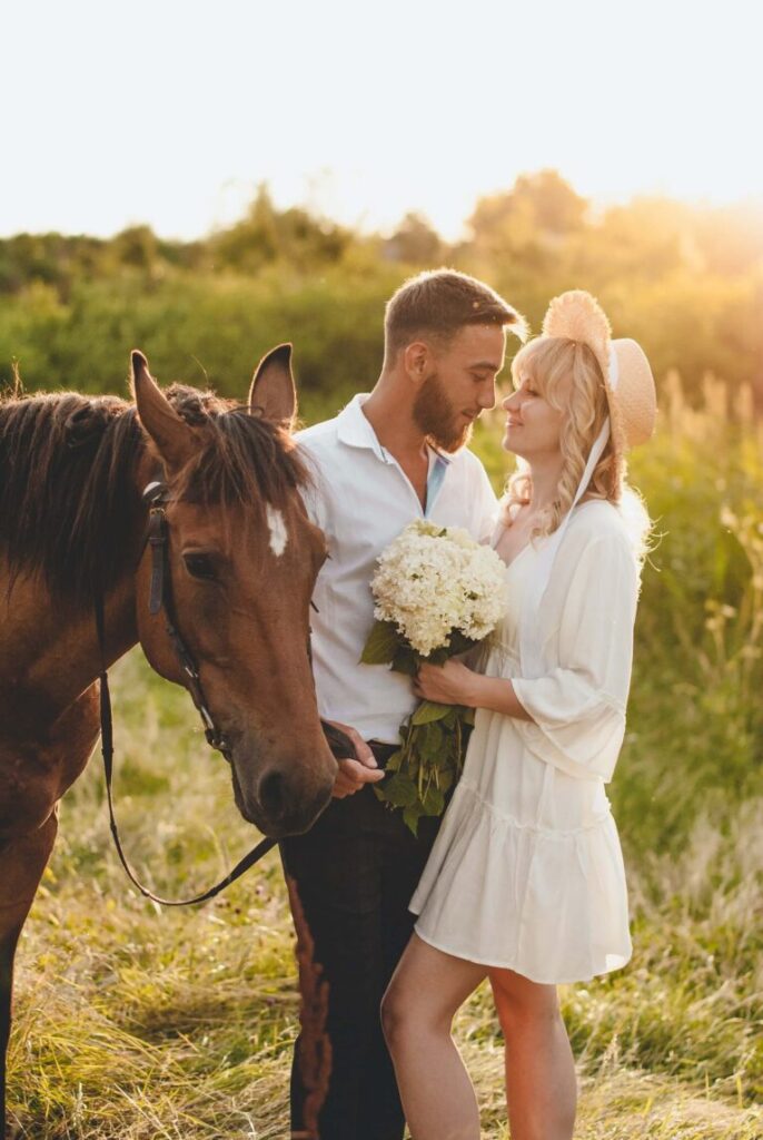 Par står nära varandra bredvid en häst i varmt kvällsljus