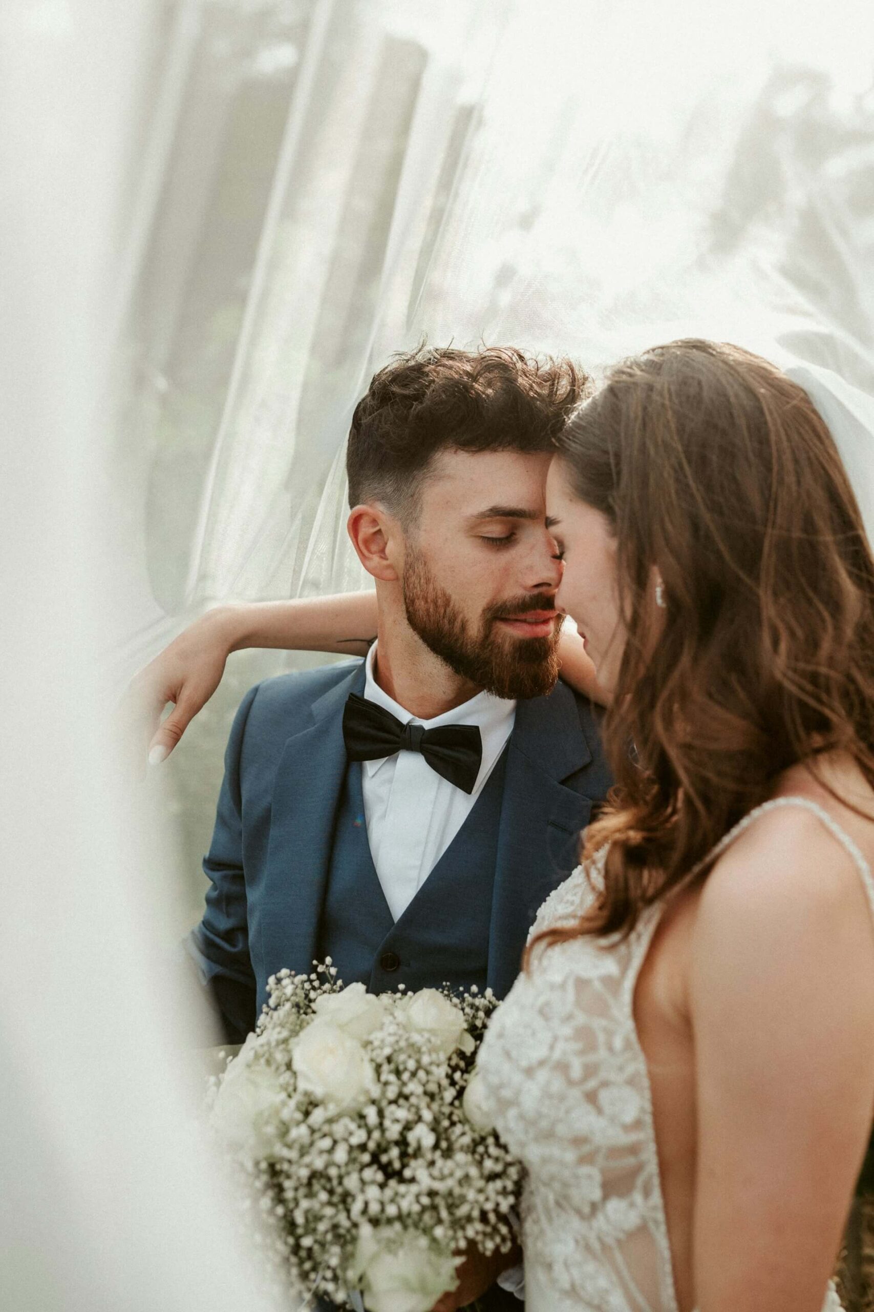 Intim närbild där brud och brudgum lutar sina pannor mot varandra bakom en mjuk slöja